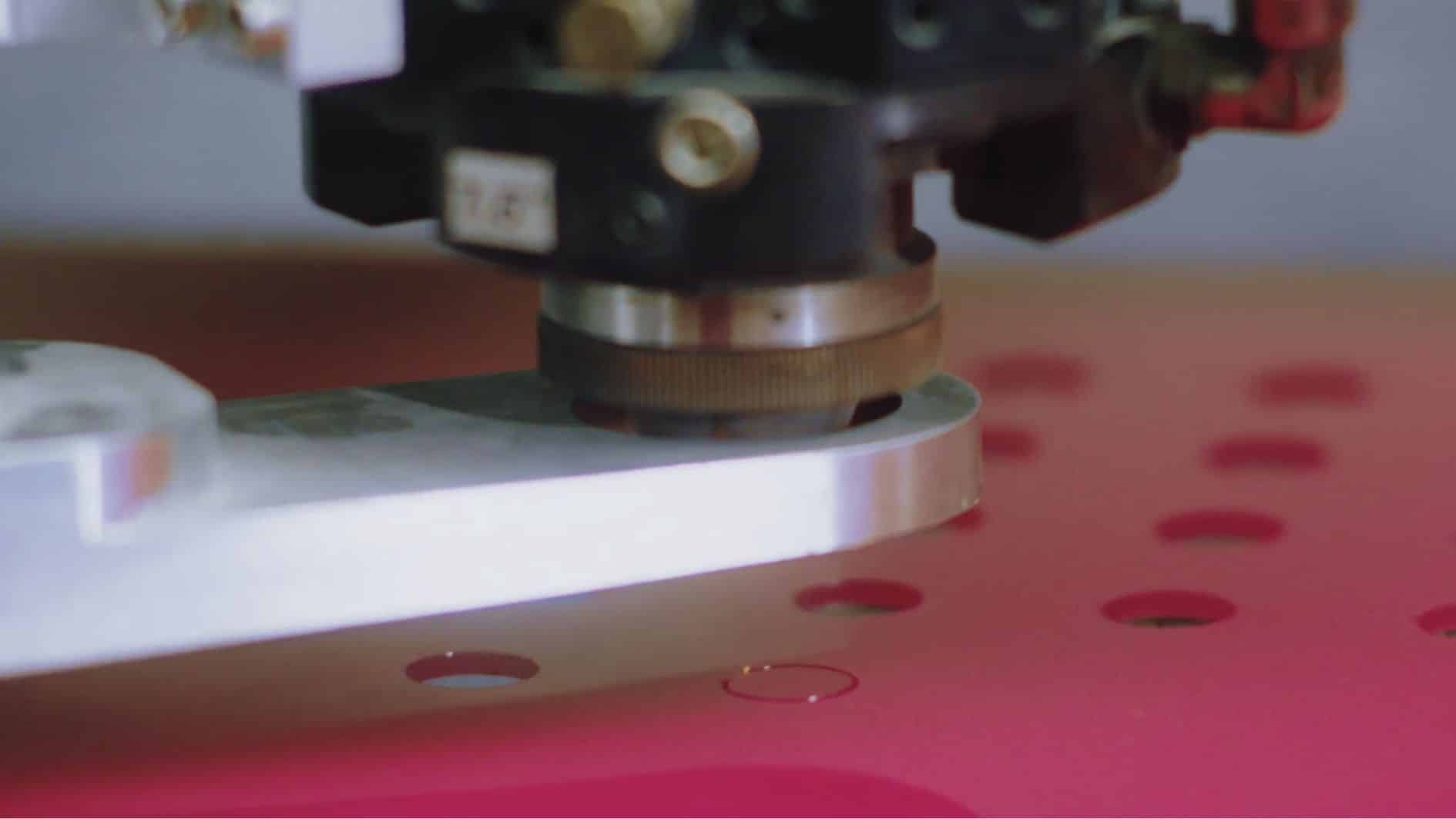 Hier zie je van dichtbij een kunststof lasermachine. De laser glijdt soepel door rozekleurig kunststofmateriaal heen.